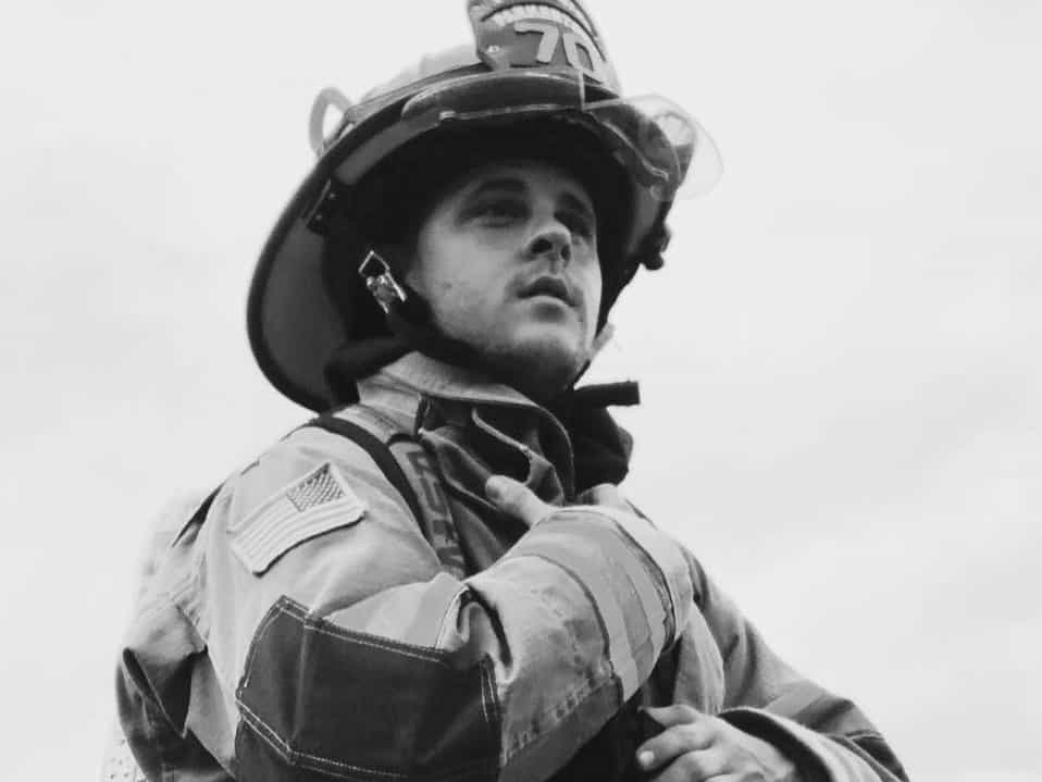 Deaf firefighter, Matt, stands in his firefighting uniform. 