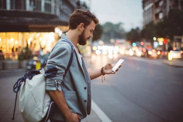 A man stands on the sidewalk looking at his CoPilot app learning about hearing therapy myths.