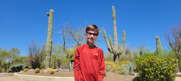 Max, a teen with microtia standing in front of cacti. 