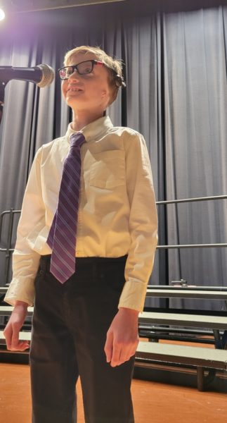 Max, a teen with microtia standing on a stage in front of a microphone