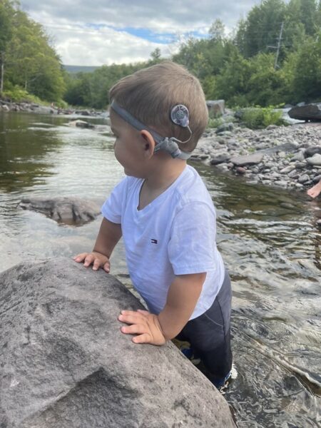 Joey who has profound hearing loss with gjb2 standing with his feet in a creek. 