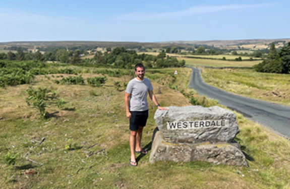 Lewis, Cochlear employee shares his story, standing next to Welcome sign of home town