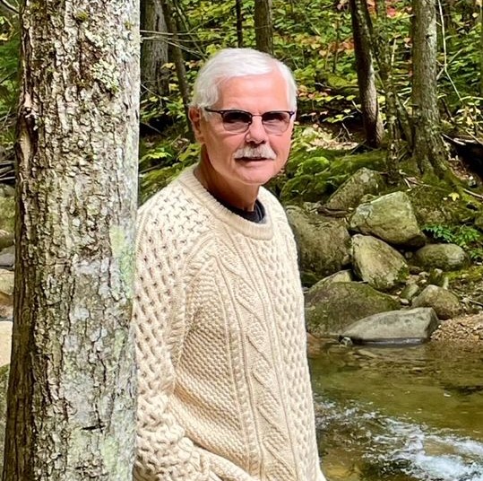 Mike, turned his hearing loss to a hearing win, posing for a photo by a creek. 
