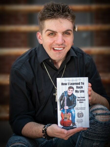 Pete, a young adult with single-sided deafness, smiling showing his book "How I Learned to Rock My Life".