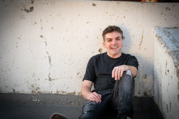 Pete, a young adult with single-sided deafness sitting against a wall, smiling.