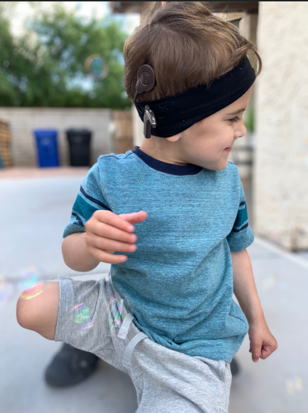 Child smiling and showing his Nucleus 8 Sound Processor with pediatric headband; keep child's hearing device on