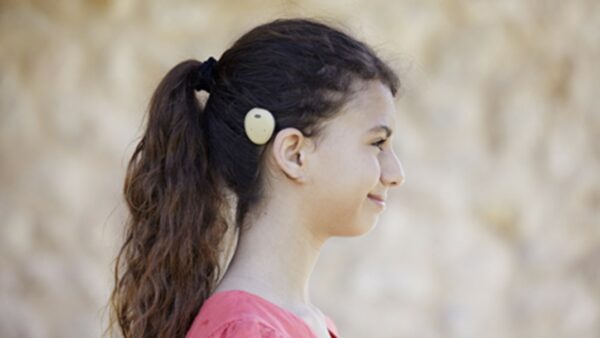 Girl showing Osia Sound Processor; practicing hearing with Baha and Osia