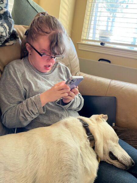 Ashley, who has an Osia Sound Processor for her conductive hearing loss, streaming sound from her phone to her device, with her dog laying on her lap. 