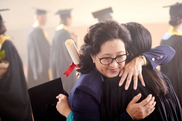Woman hugging graduate controlling hearing devices with the Nucleus Smart App