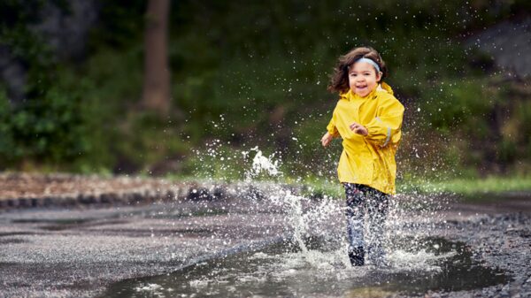 Little girl wearing yellow rain coat outside, splashing in the puddles; sound processor rated