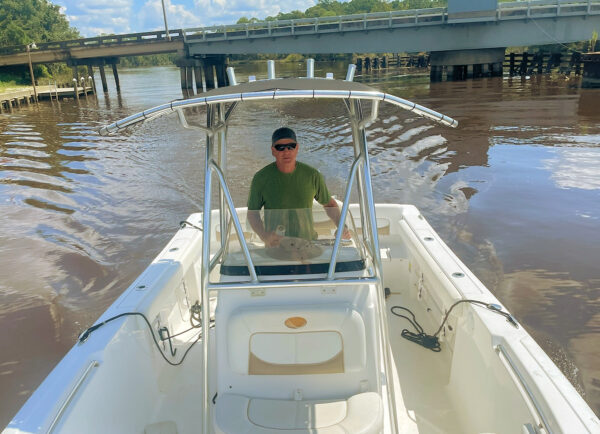 Eric, who has progressive sensorineural hearing loss, standing at the steering wheel of a boat and driving. 