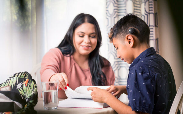 Madre e hijo sentados en una mesa leyendo un libro; recursos-usuarios-español