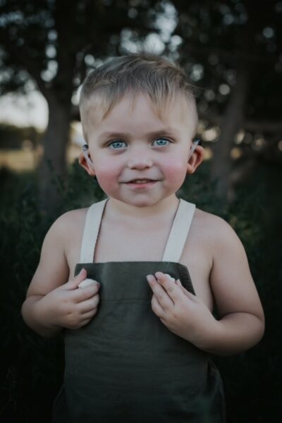 Gramm, a child with bilateral hearing loss, posing for a picture with his cochlear implants on each ear. 