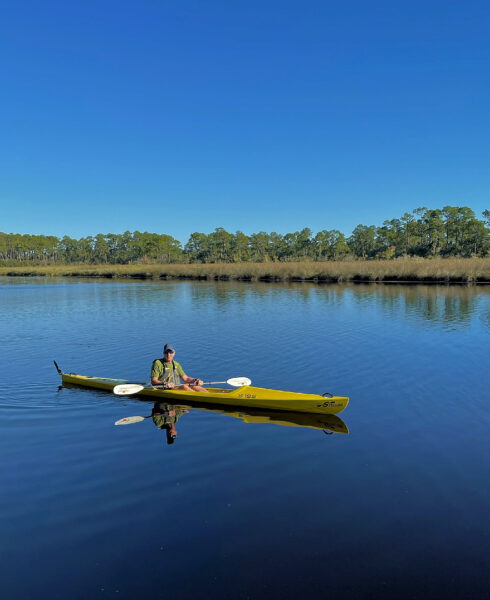 Eric, who has progressive sensorineural hearing loss, kayaking in a lake with trees in the background. 