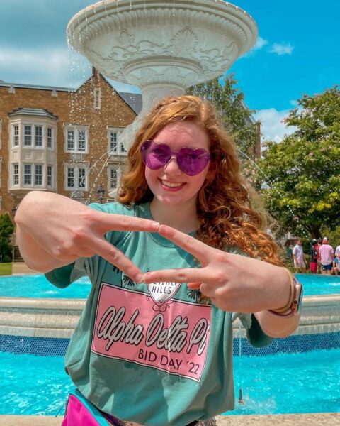 Born profoundly deaf in both ears, Riley poses in front of a fountain holding up the symbol on her hands for her sorority. 