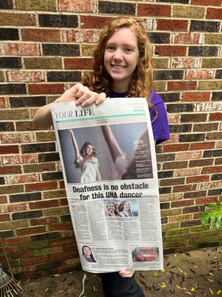 Born profoundly deaf in both ears, Riley poses with a local newspaper showing an article on her and her life.