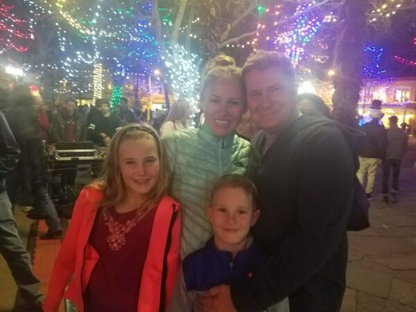 Tiffany, who shares her tips for hearing during the holidays with a cochlear implant, posing with her family surrounded by Christmas lights. 