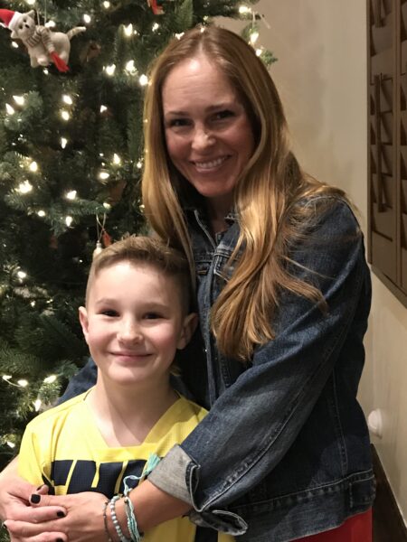 Tiffany, who shares her tips for hearing during the holidays with a cochlear implant, posing by a Christmas tree holding her son. 