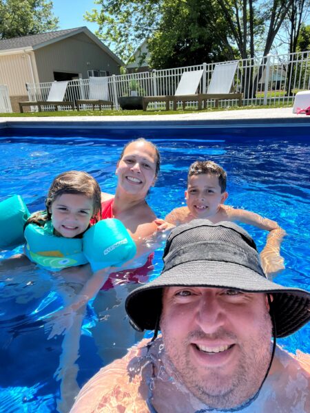 Mark and Tate who experience hereditary hearing loss taking a picture swimming in a pool with their family. 