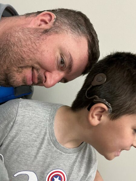 Mark and Tate who experience hereditary hearing loss, posing for a photo with their sound processors showing to the camera. 