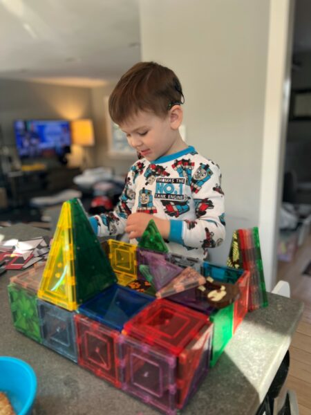 Theo who is a toddler with hearing loss, playing with building blocks in his house with his cochlear implant on his ear. 