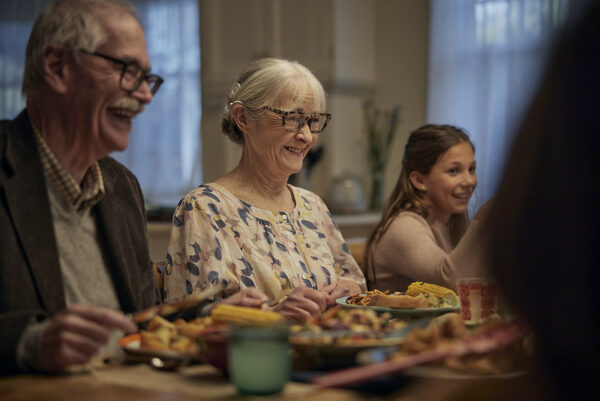 A photo of a mature adult woman with her family at the dinner table to help describe conductive vs sensorineural hearing loss. 