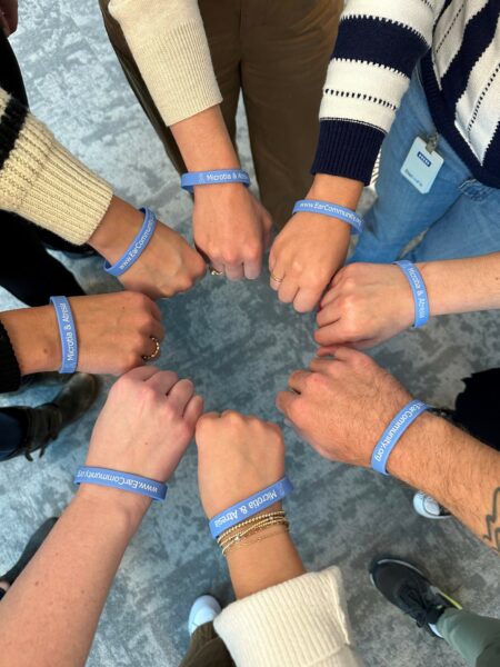 A group of Ear Community activists forming a circle out of their hands with bracelets supporting Microtia & Atresia Awareness Day. 