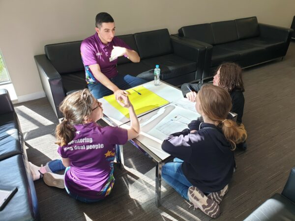 A mentor sitting down and mentoring 3 teens with hearing loss