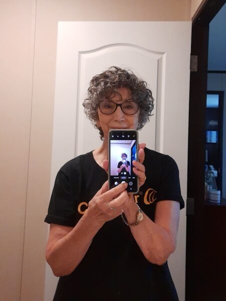 Donna Sue, who has a Baha System for SSD, taking a picture with her cell phone wearing a Cochlear t-shirt. 