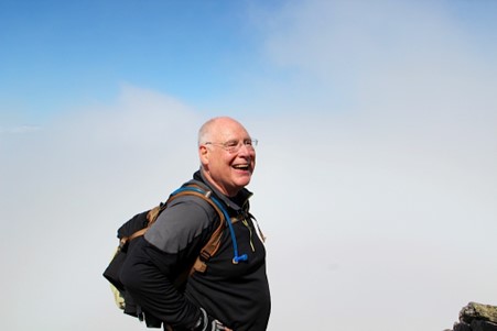 Peter, a cochlear implant recipient, who is backpacking and smiling at the camera. Learn more about your over 50 hearing screening checklist.