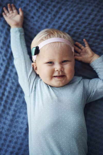 Baby girl smiling with her Baha 6 Max Sound Processor on a pink headband; Baha Ponto System.