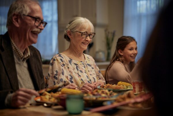 A picture of an older female cochlear implant recipient sitting at the dinner table with her family and smiling. A cochlear implant is a solution for sensorineural hearing loss for those who are qualified candidates. 