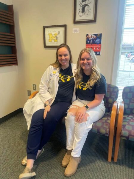 Morgan, a deaf young woman who has cochlear implants, posing for a picture sitting with her Audiologist Dr. Rachel Fryatt and the University of Michigan Clinic. 