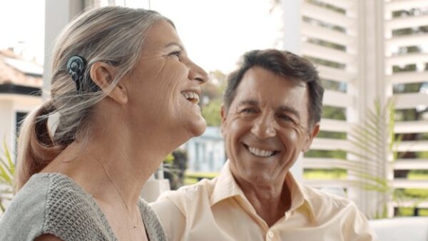 Woman smiling having a conversation with husband, showing her Cochlear™ Nucleus® 8 Sound Processor; favorite hearing resources