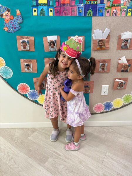 Sophie & Leah, whose parents noticed signs of hearing loss, smiling and posing for a photo together at school.