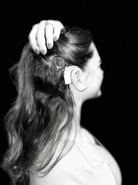 Mia, who was diagnosed with bilateral profound deafness, in a black and white photo of her holding her hair up, to show off her sound processor. 