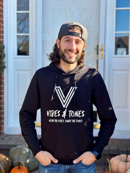 Peter, who has the Osia Sound Processor, taking a picture in front of a porch with a hoody representing his awareness company - Vibes & Tones. 