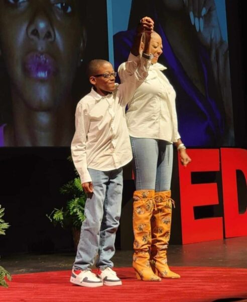 Kay, who experienced hearing loss from addiction, shown with her fingers laced with her child's on stage, after completing her TEDx Speech. 