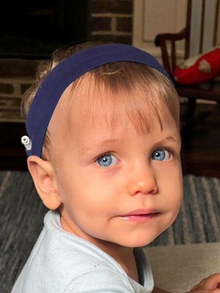 Jamie, a young child who received a cochlear implants to support his hearing health, posing for a picture, wearing a headband with his sound processor showing. 