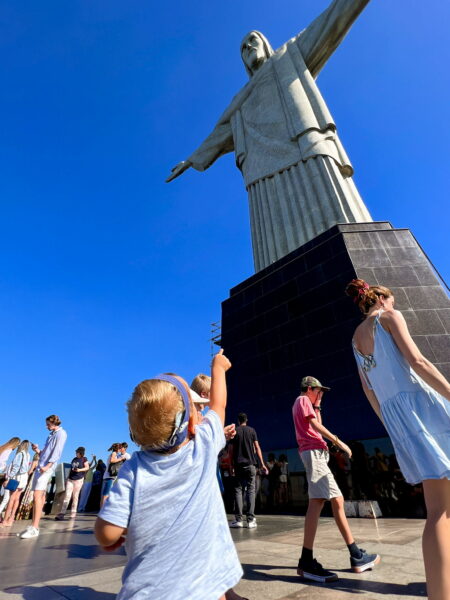 Jamie, a child who received cochlear implants to support his hearing health standing underneath and pointing to up at the Christ the Redeemer statue in Brazil. 