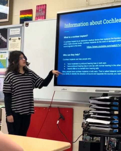 Hannah stands at the front of the classroom presenting on information about cochlear implant. Her mom shares her knowledge about back to school time.