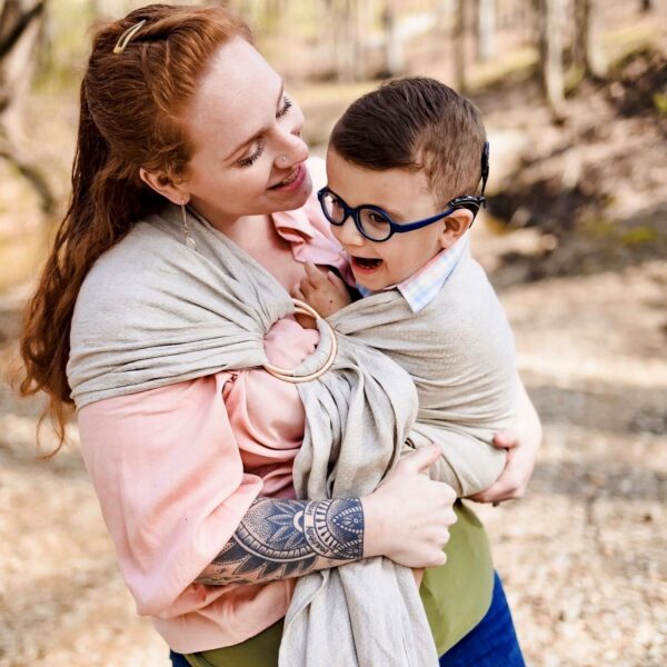 Liam, a young boy with cochlear implants who used speech therapy to make progress in his life, being held in a shawl and laughing with his mother. 