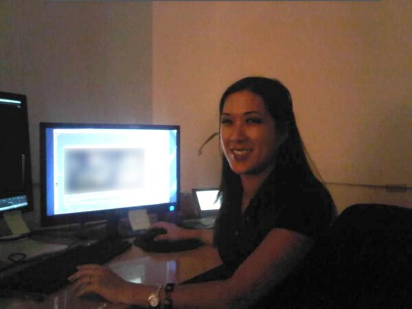 Amy, who uses the Cochlear Kanso Sound Processor, smiling while sitting in front of two computer screens. 