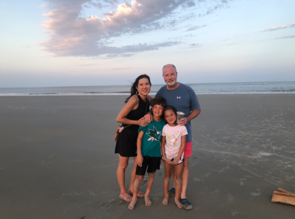 Amy, who uses the Cochlear Kanso Sound Processor smiling for a photo on a beach with her husband, son and daughter. 