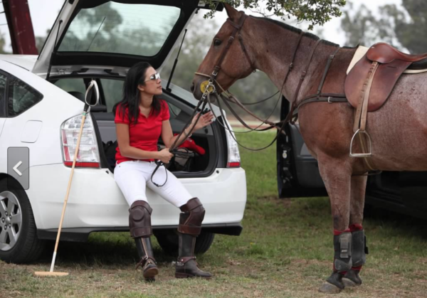 Amy, whose use of the Cochlear Kanso Sound Processor has helped her, sitting on the back of an open car, holding a horse by the reins. 