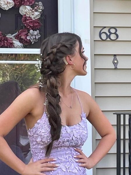 Trysta, who aspires to be an audiologist from her experience with her cochlear implants, posing in an elegant dress with her hair braided, showing off one of her cochlear implants. 