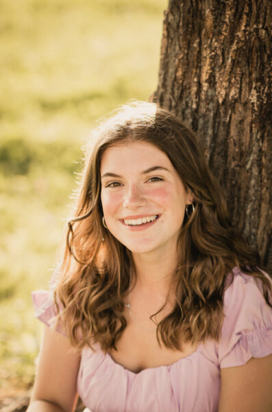 Trysta, who aspires to be an audiologist from her experience with her cochlear implants, posing for a professional photo under a tree with sunlight streaming through. 