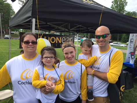 A picture of Trysta, who aspires to be an audiologist based on her experience with her cochlear implants, posing for a family photo in front of a Cochlear tent at a Walk4Hearing event. 