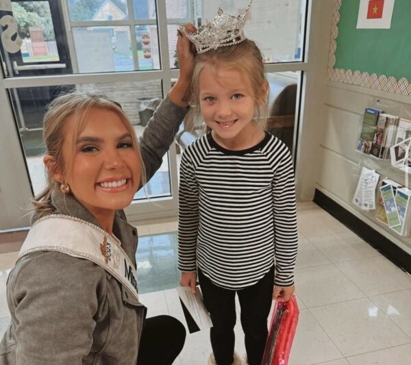 Brielle, a girl with a cochlear implant, shown smiling for a photo with fellow Osia System recipient Vanessa Munson, who is Miss Washington. Vanessa is placing a tiara on Brielle's head for the photo. 