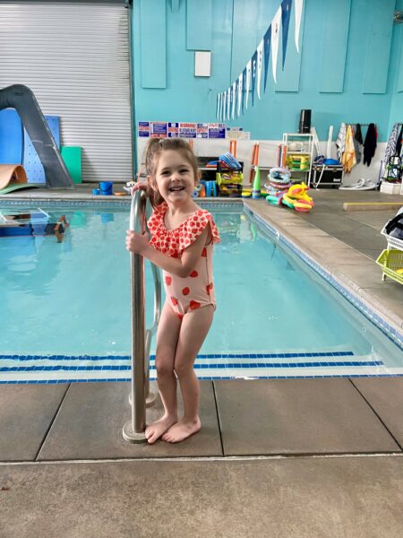 Willow, a child diagnosed with Waardenburg syndrome, shown standing by a swimming pool and smiling as she poses for a photo. 